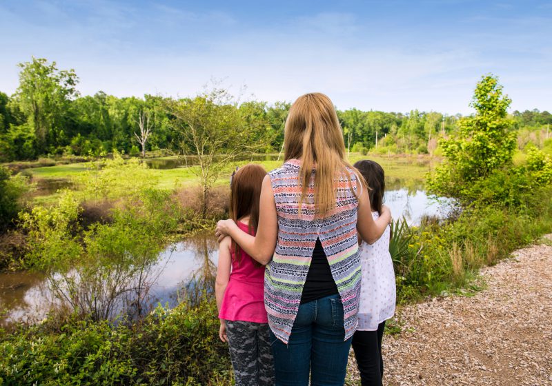 A woman and two girls standing in front of pond.